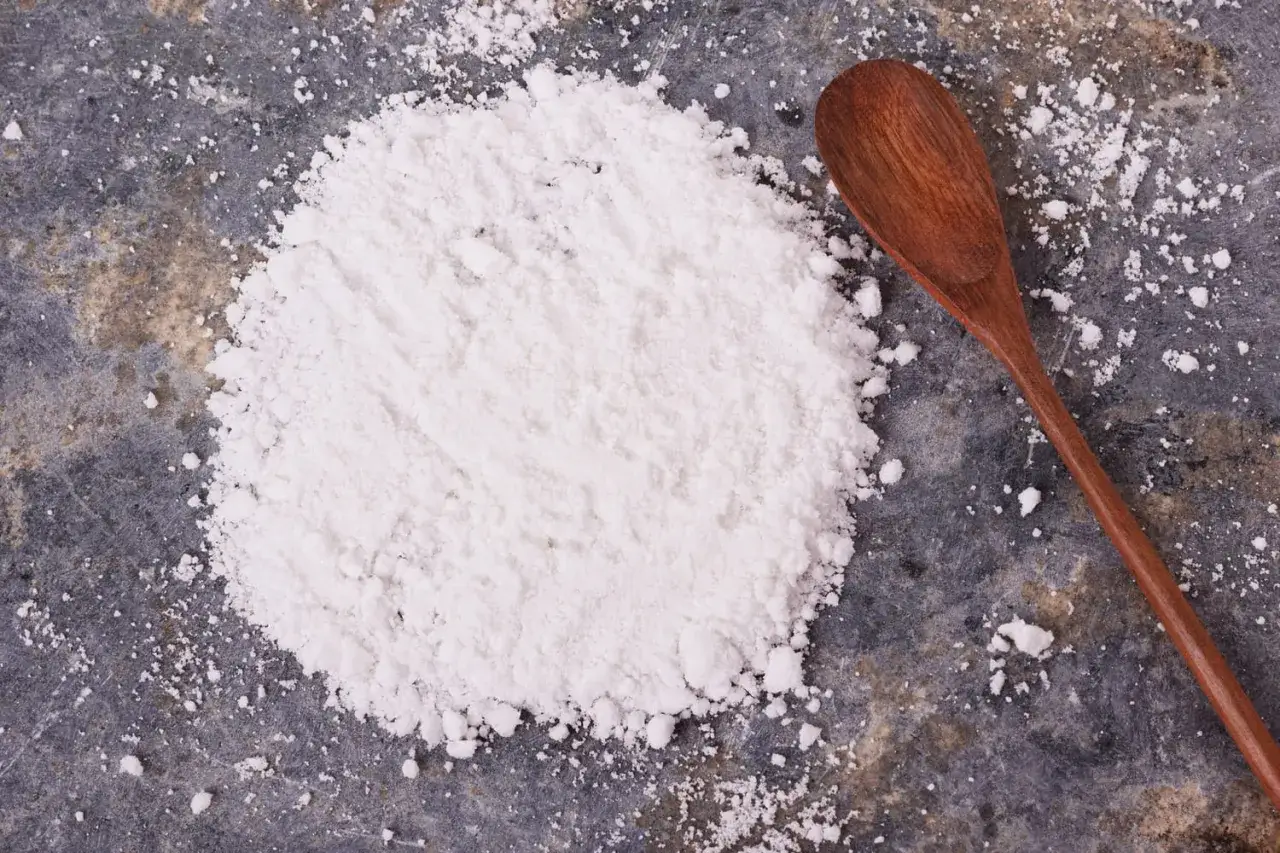 Une cuillère en bois repose près d'une poudre blanche, idéale par quoi remplacer la fécule de pomme de terre pour épaissir vos sauces.