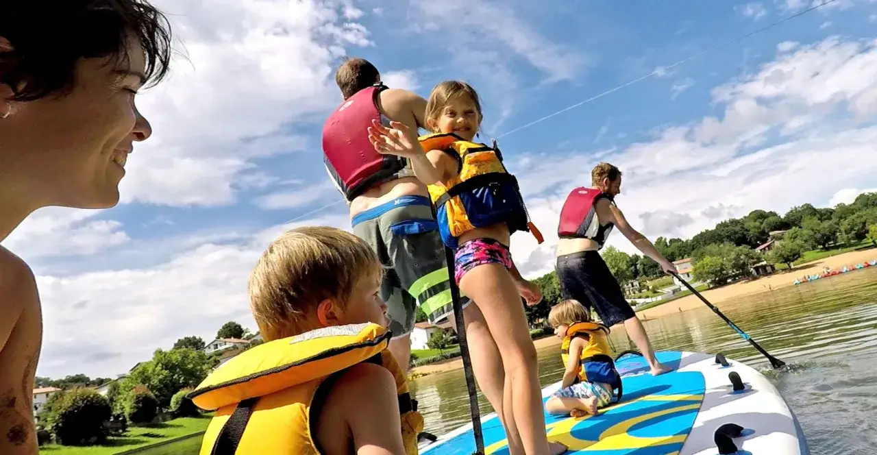 Familia disfrutando del paddle surf en el País Vasco con niños. Días soleados y risas en el agua.