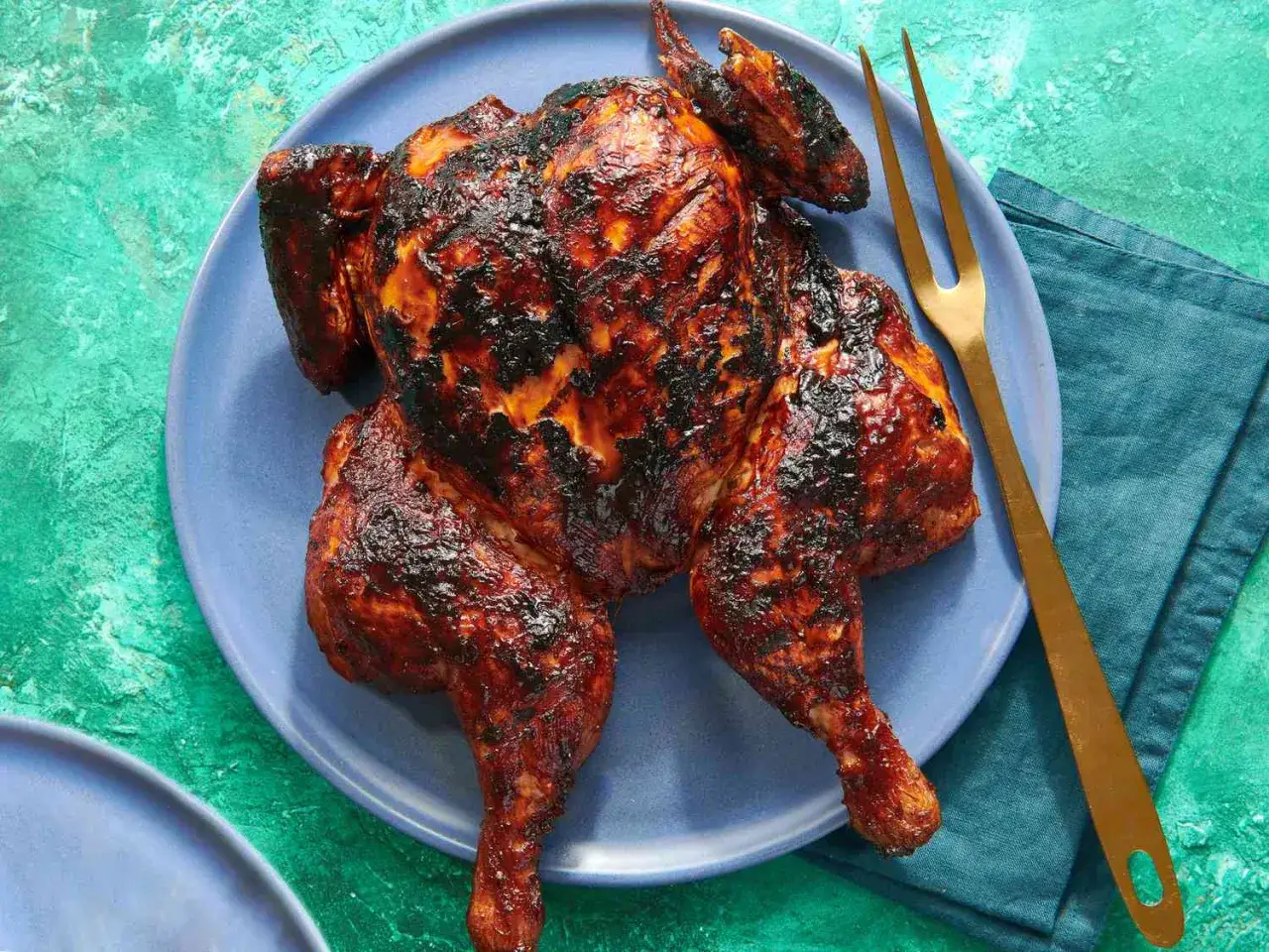 Helstekt kyckling med härlig kycklingmarinad bbq, serverad på en blå tallrik med en guldig gaffel.