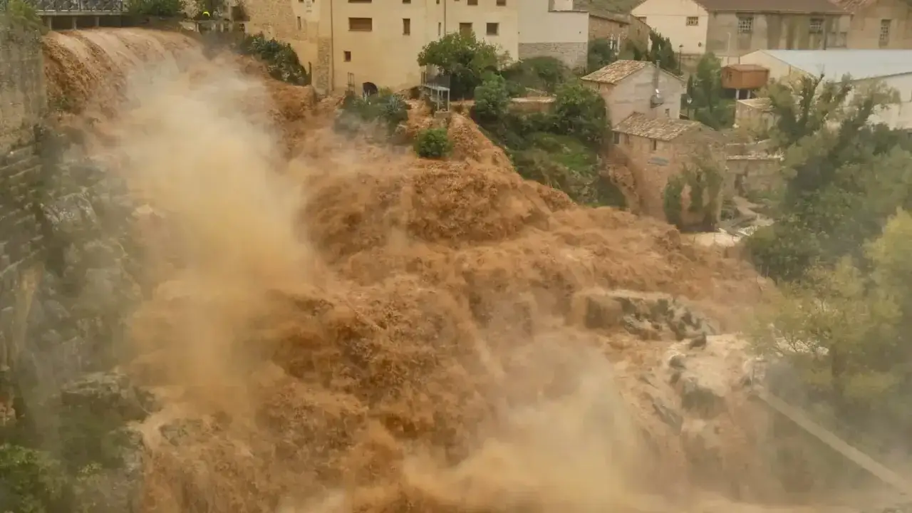 El río desbordado arrastra lodo y agua turbia por el pueblo de Almonacid de la Cuba, creando una cascada marrón.