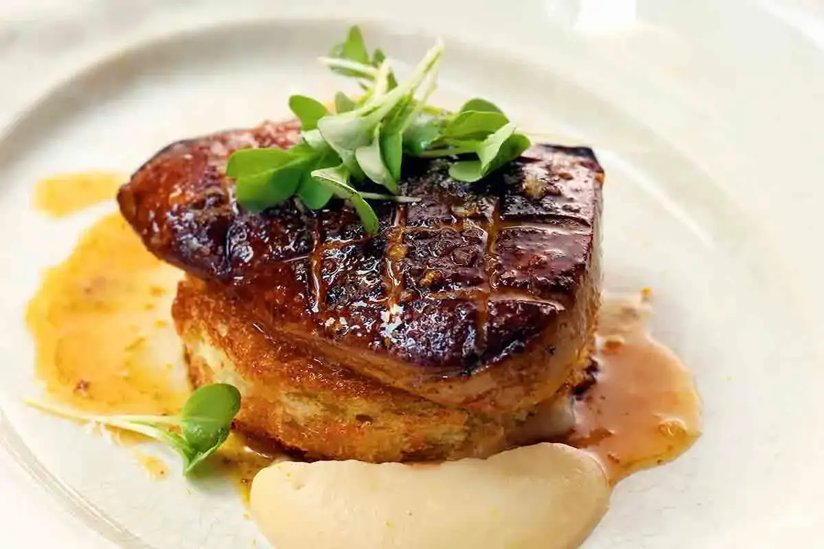 Deliciosa tosta de foie a la plancha, dorada y jugosa, sobre pan tostado, con salsa y brotes verdes.