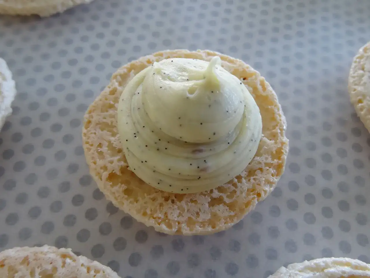 Un macaron vanille garni d'une crème onctueuse parsemée de graines de pavot.