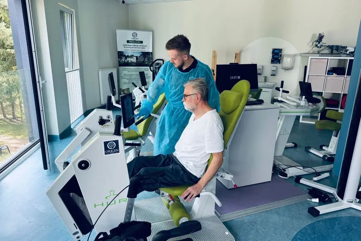 Rehabilitacja po chorobie Parkinsona. Fizjoterapeuta pomaga pacjentowi na siłowni. Długość życia z parkinsonem zależy od wielu czynnik&oacute;w.