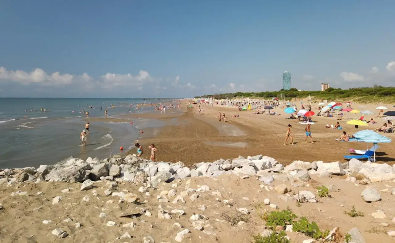Plage anim&eacute;e &agrave; Lido di Jesolo, avec des baigneurs dans l'eau et sur le sable, sous des parasols color&eacute;s.