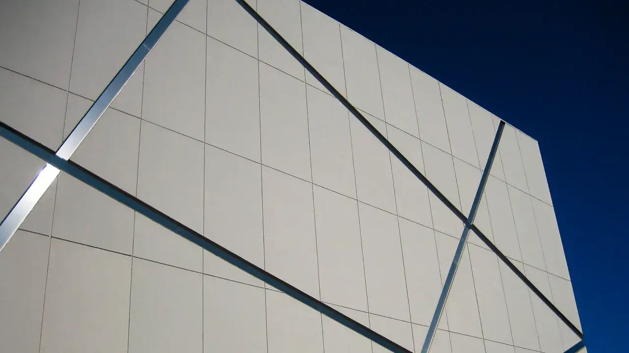 Fachada moderna con paneles de pladur para exterior, unidos por perfiles met&aacute;licos, contra un cielo azul intenso.