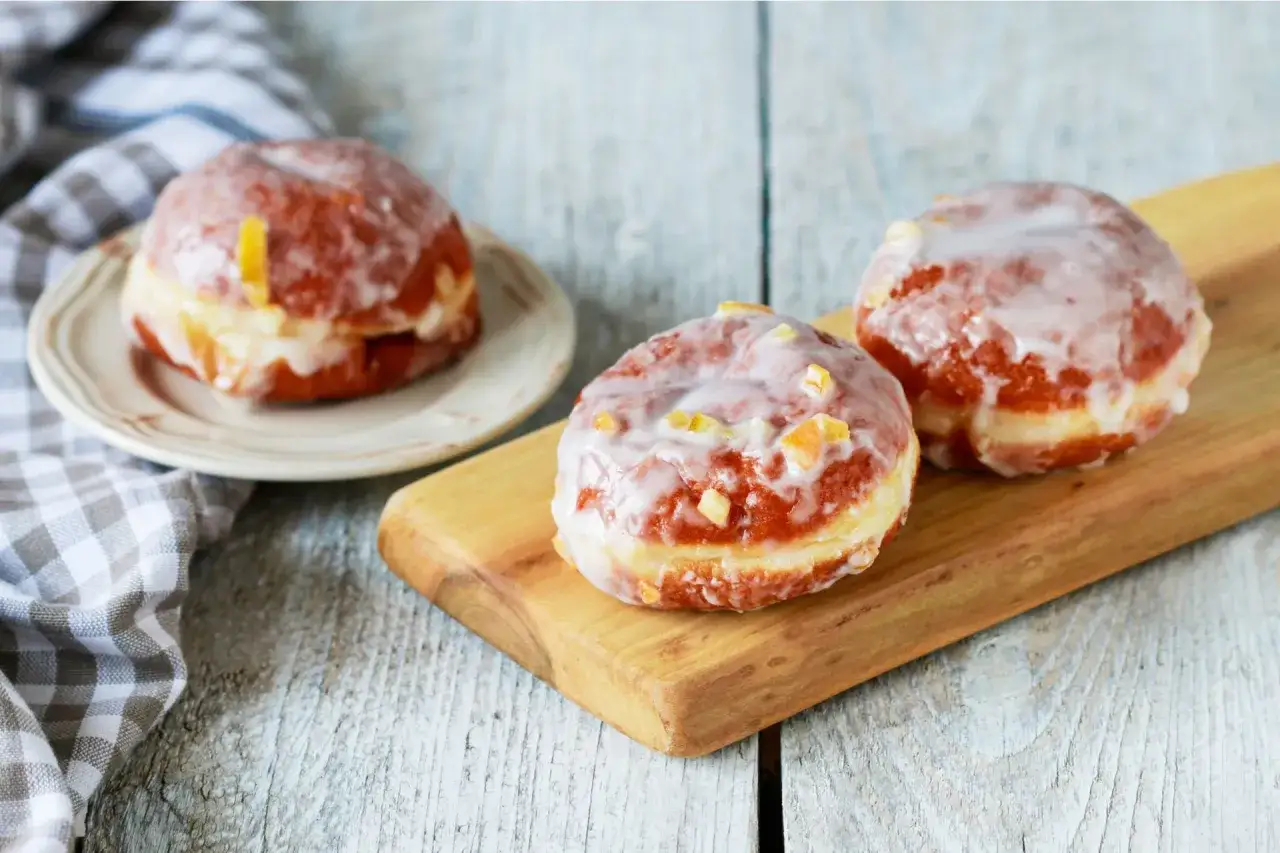 Pączki z lukrem do pączków, ozdobione kandyzowaną skórką pomarańczową, kuszą na drewnianej desce i talerzyku.