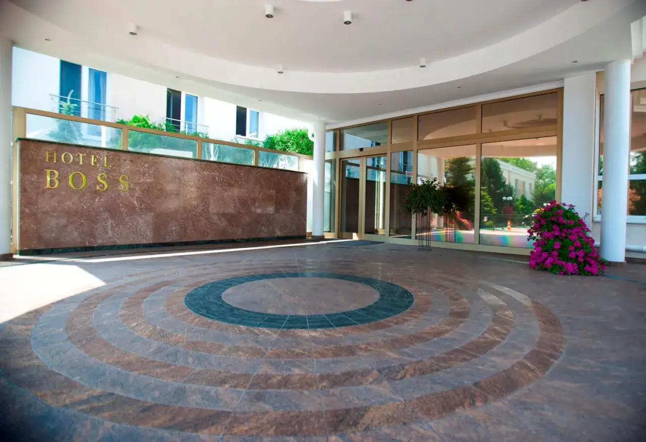 Eleganckie wejście do jednego z polskich hoteli niezależnych, Hotel Boss. Marmurowa ściana z logo, szklane drzwi i kolorowe kwiaty.