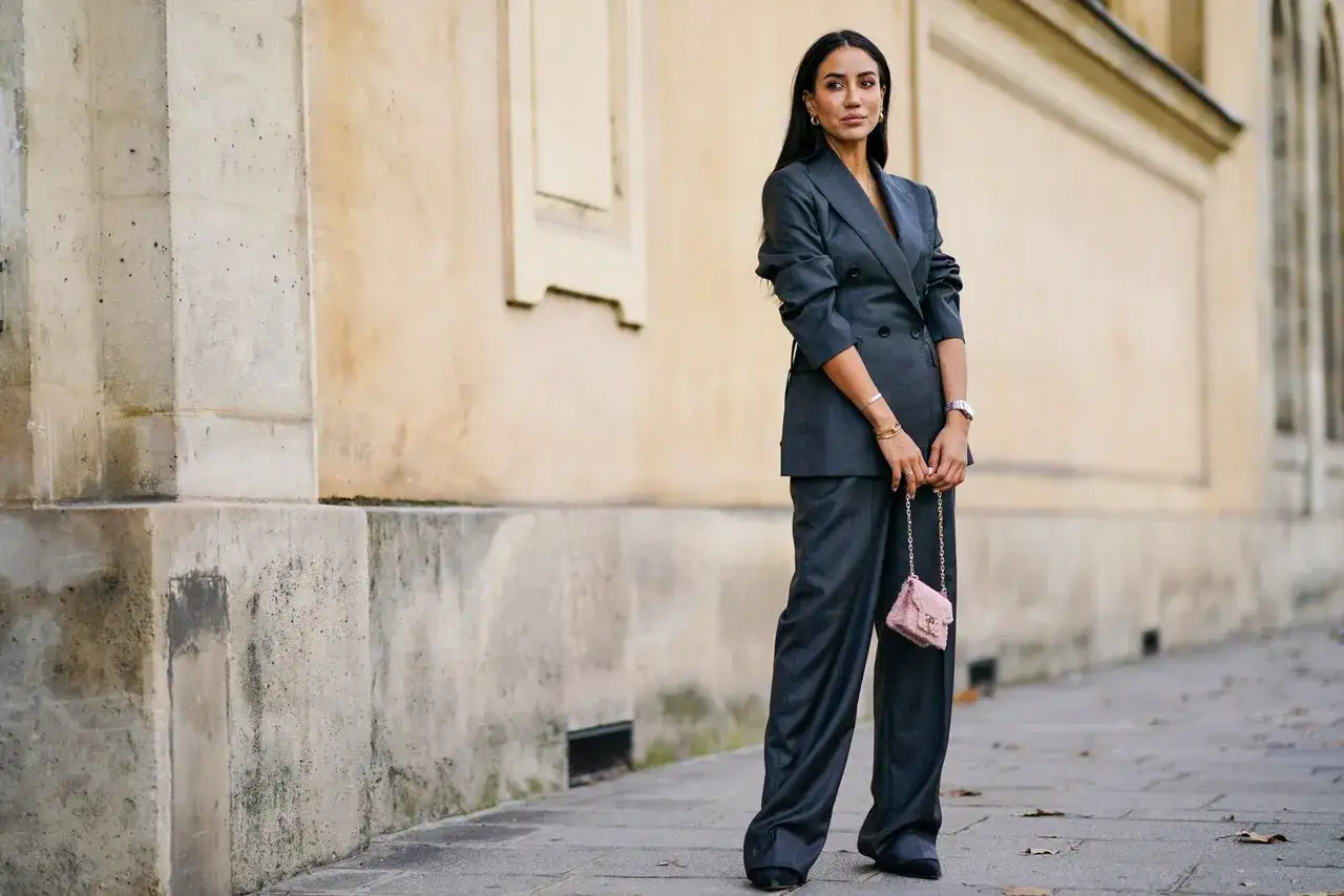 Elegancka kobieta w garniturze w kolorze gołębim, z różową torebką na łańcuszku.