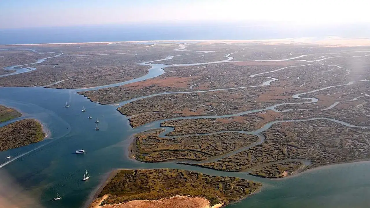 Luftaufnahme des Ria Formosa Nationalparks mit seinen verschlungenen Wasserwegen und Salzwiesen. Boote segeln auf dem ruhigen Wasser.