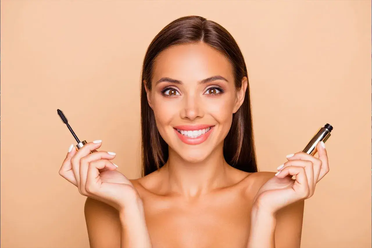 Une femme souriante tient un mascara, pr&ecirc;te &agrave; apprendre comment mettre du mascara pour un regard intense.