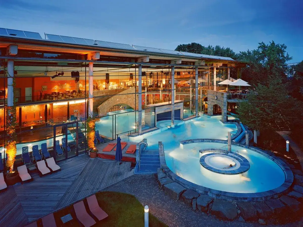 Entspannter Abend in einer modernen Therme NRW mit beleuchteten Pools, Rutschen und Liegen.
