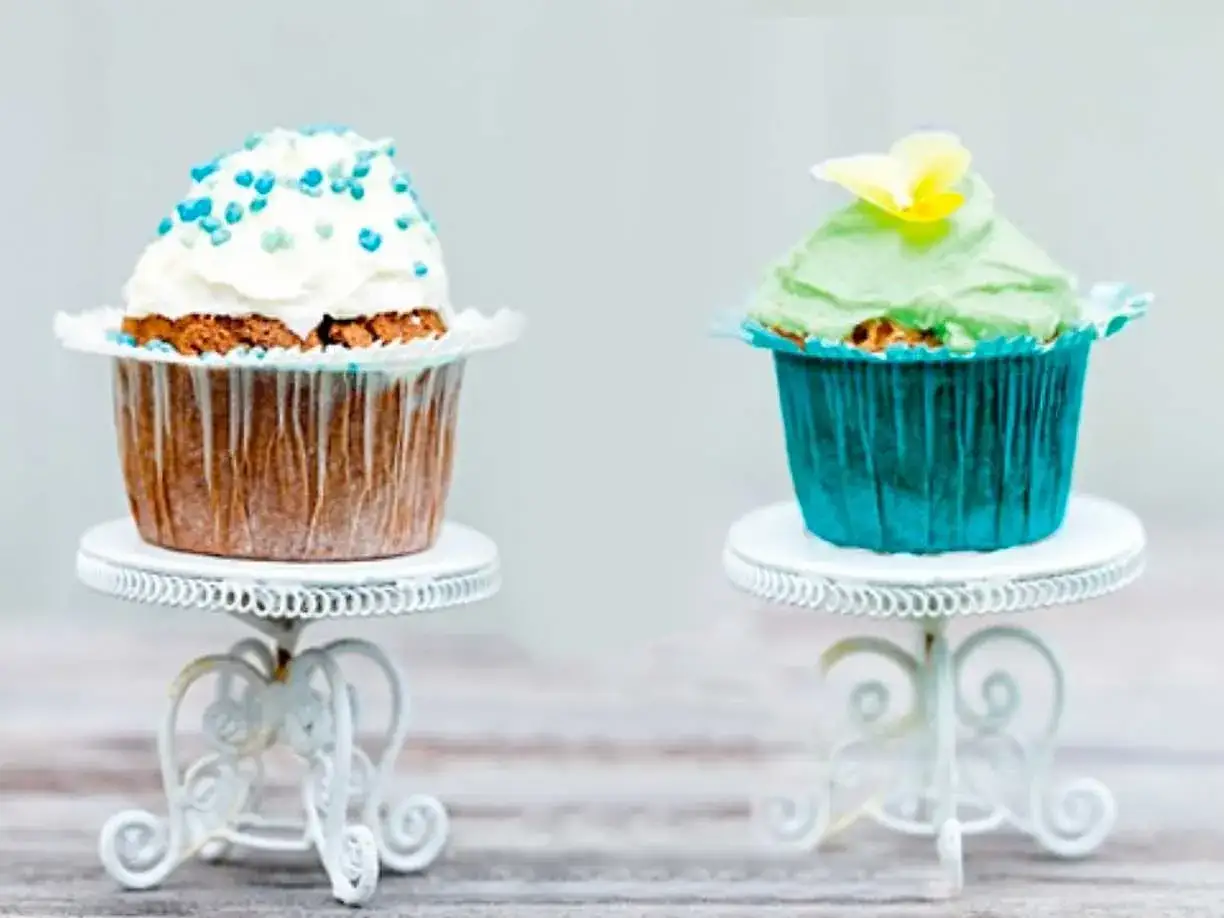 Tv&aring; glutenfria kladdkakemuffins, en med vit frosting och bl&aring; str&ouml;ssel, den andra med gr&ouml;n frosting och en gul blomma.