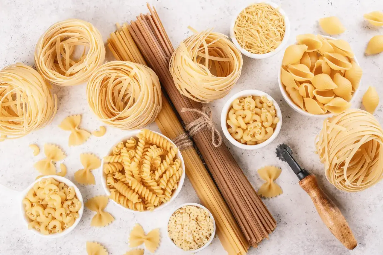 Różnorodne dania z makaronem: tagliatelle, fusilli, muszelki, farfalle i inne, ułożone na jasnym tle.
