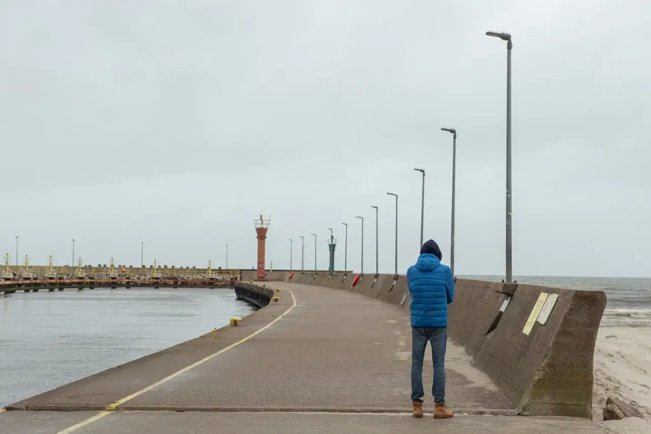 Samotny spacer po łebskiej promenadzie. W oddali widać latarnie morskie i falochrony.