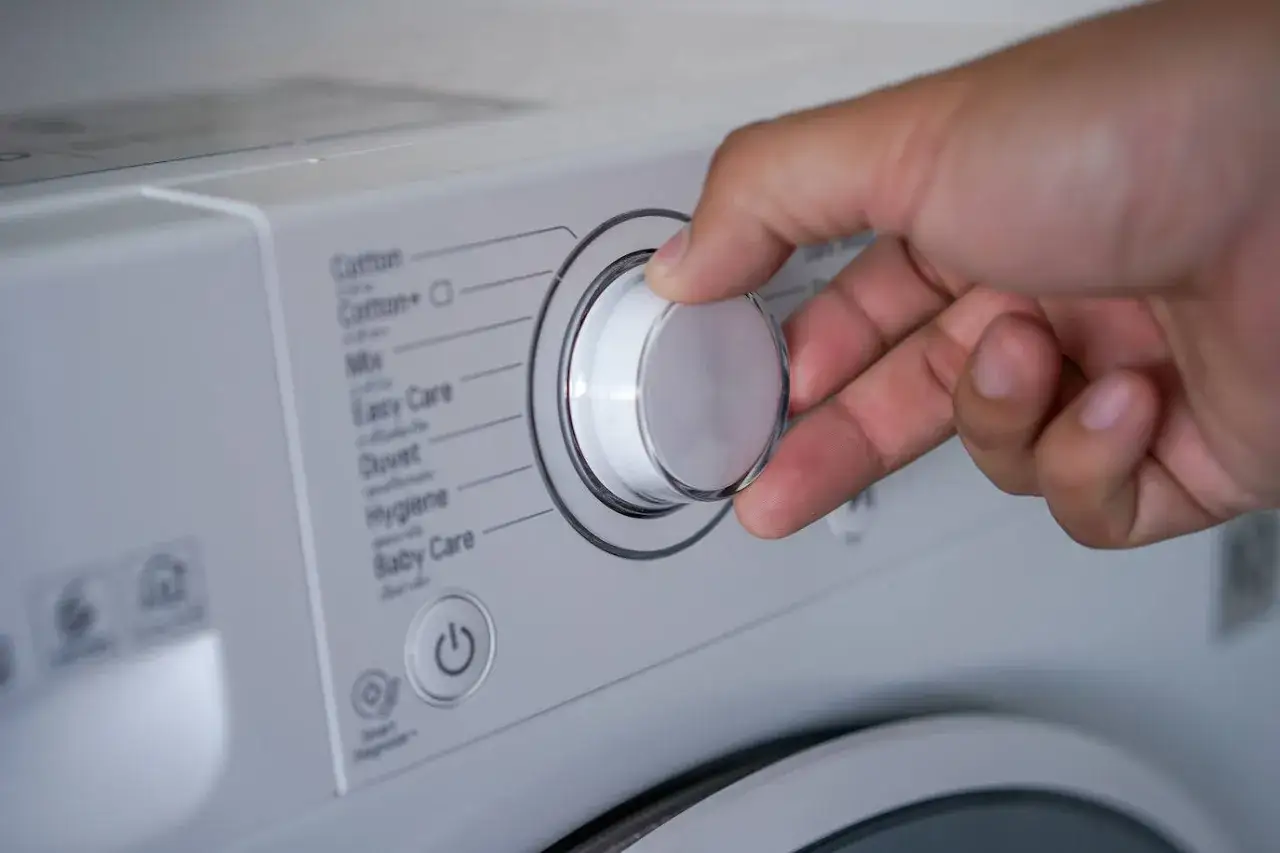 Mano ajustando el selector de la lavadora para saber como lavar un anorak. Se ven programas como