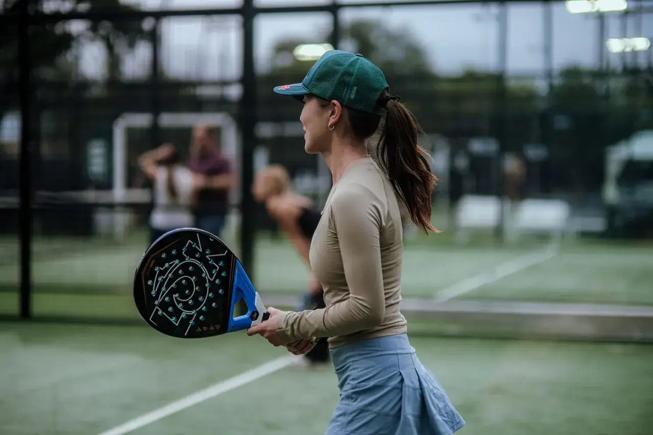 Donna con cappellino e racchetta da padel, pronta a giocare. L'abbigliamento ideale per giocare a padel è comodo e traspirante.