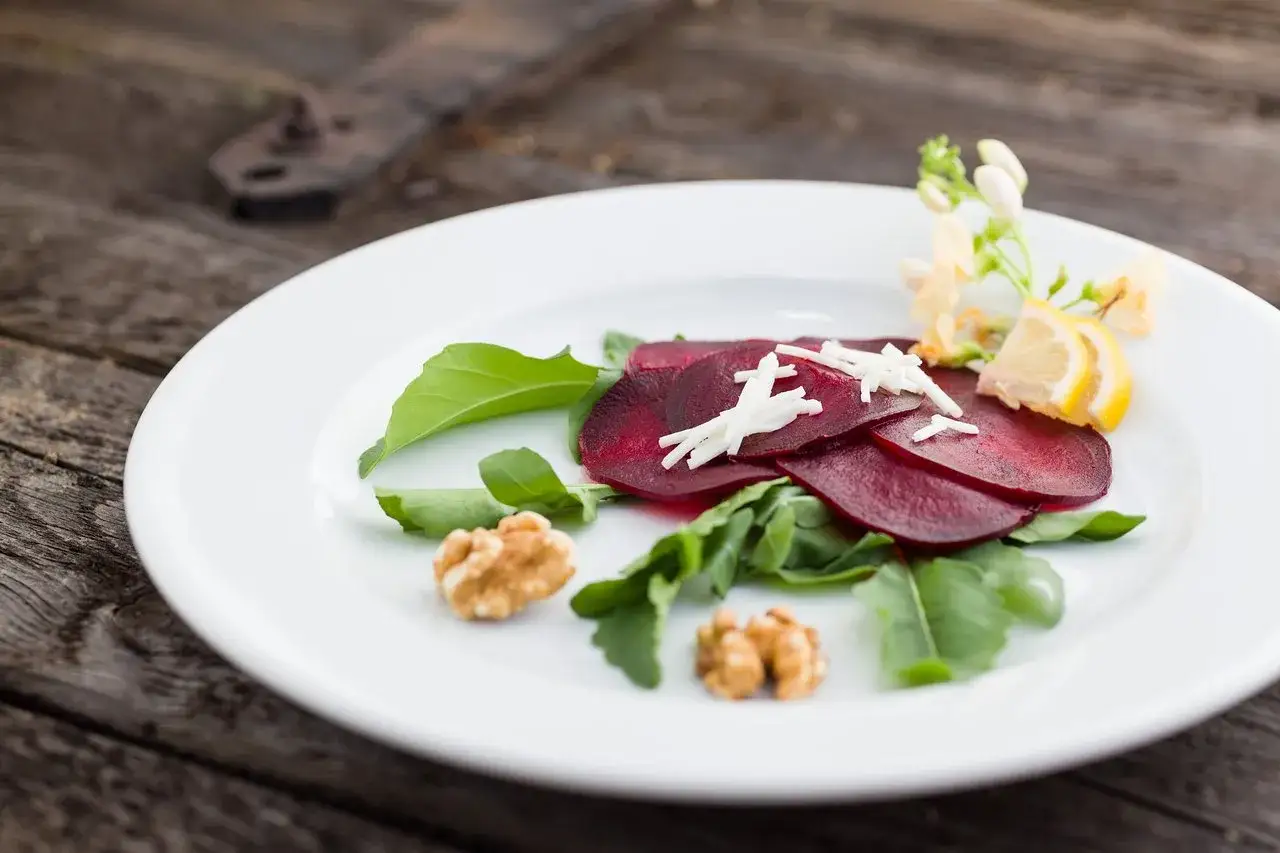 Eleganckie carpaccio z buraka z rukolą, orzechami, serem i cytryną na białym talerzu.