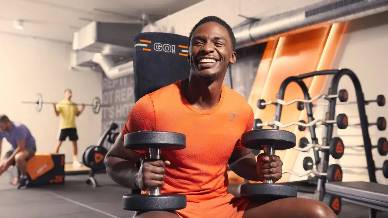 Hombre sonriente en gimnasio con mancuernas. Pregúntate cuanto tarda en hacer efecto la creatina mientras entrenas.