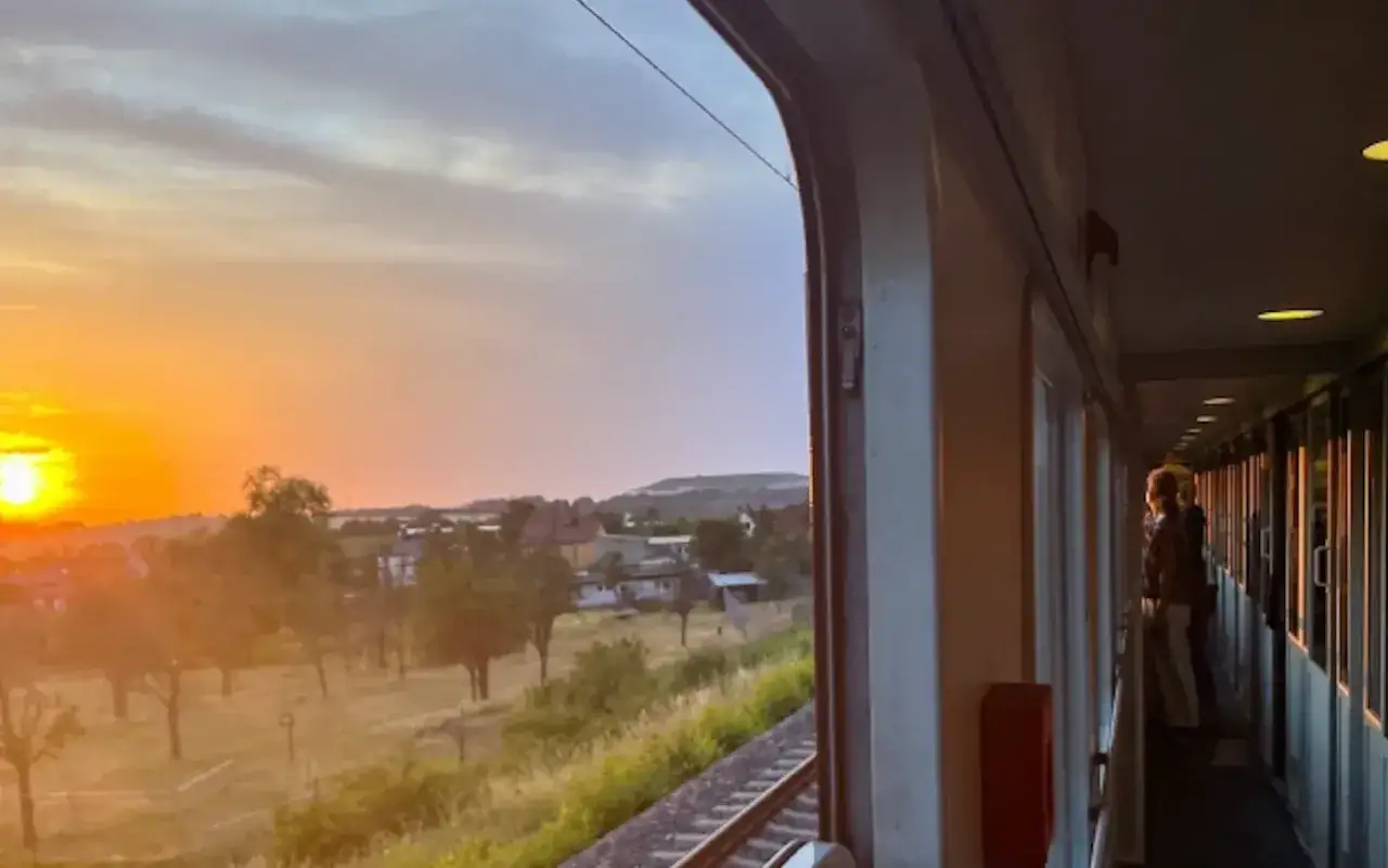 Sunset view from a train from AMS to Brussels. Two people stand in the train's corridor, looking out at the golden sky and passing countryside.