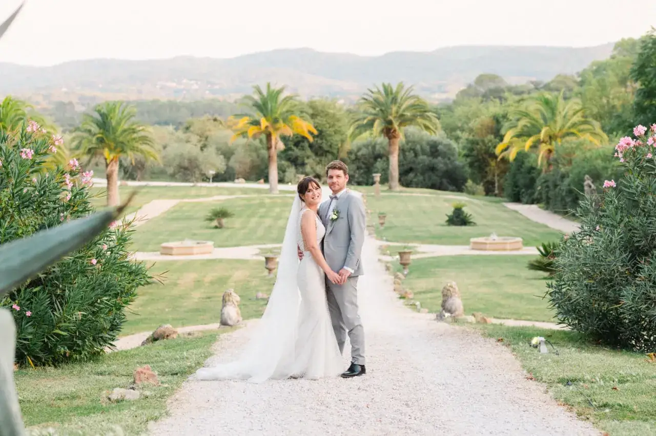 Un couple heureux lors d'une photographie de mariage, entouré d'un jardin luxuriant avec des palmiers et des collines en arrière-plan.