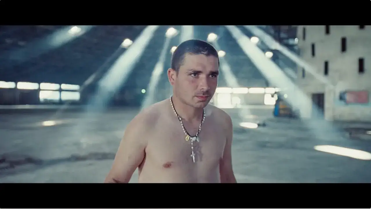 Mężczyzna w naszyjniku z krzyżem, w opuszczonej hali, jak z teledysku Paolo Nutini Iron Sky.