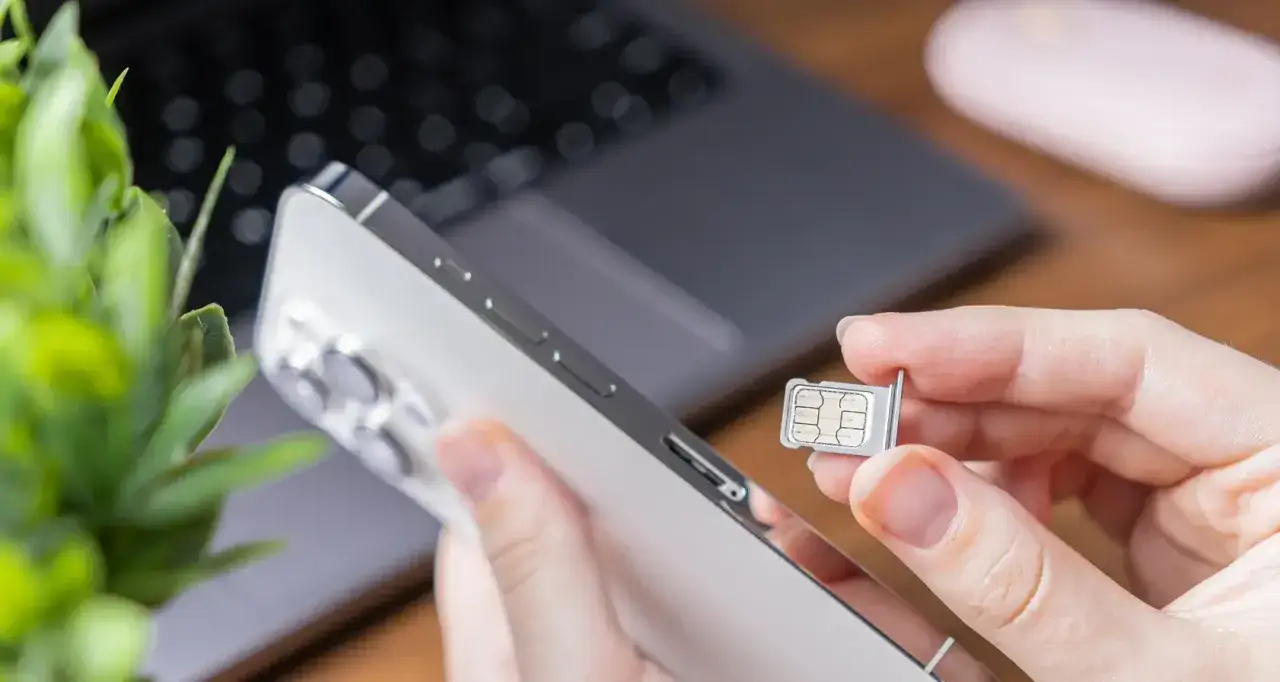 Une main insère une carte SIM physique dans un smartphone.
