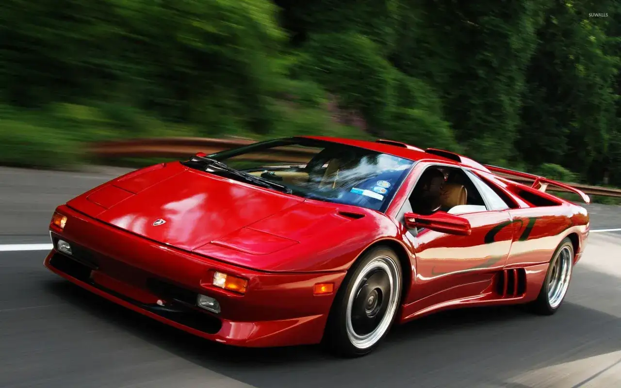 Czerwony Lamborghini Diablo pędzi po krętej drodze, otoczony zielenią.