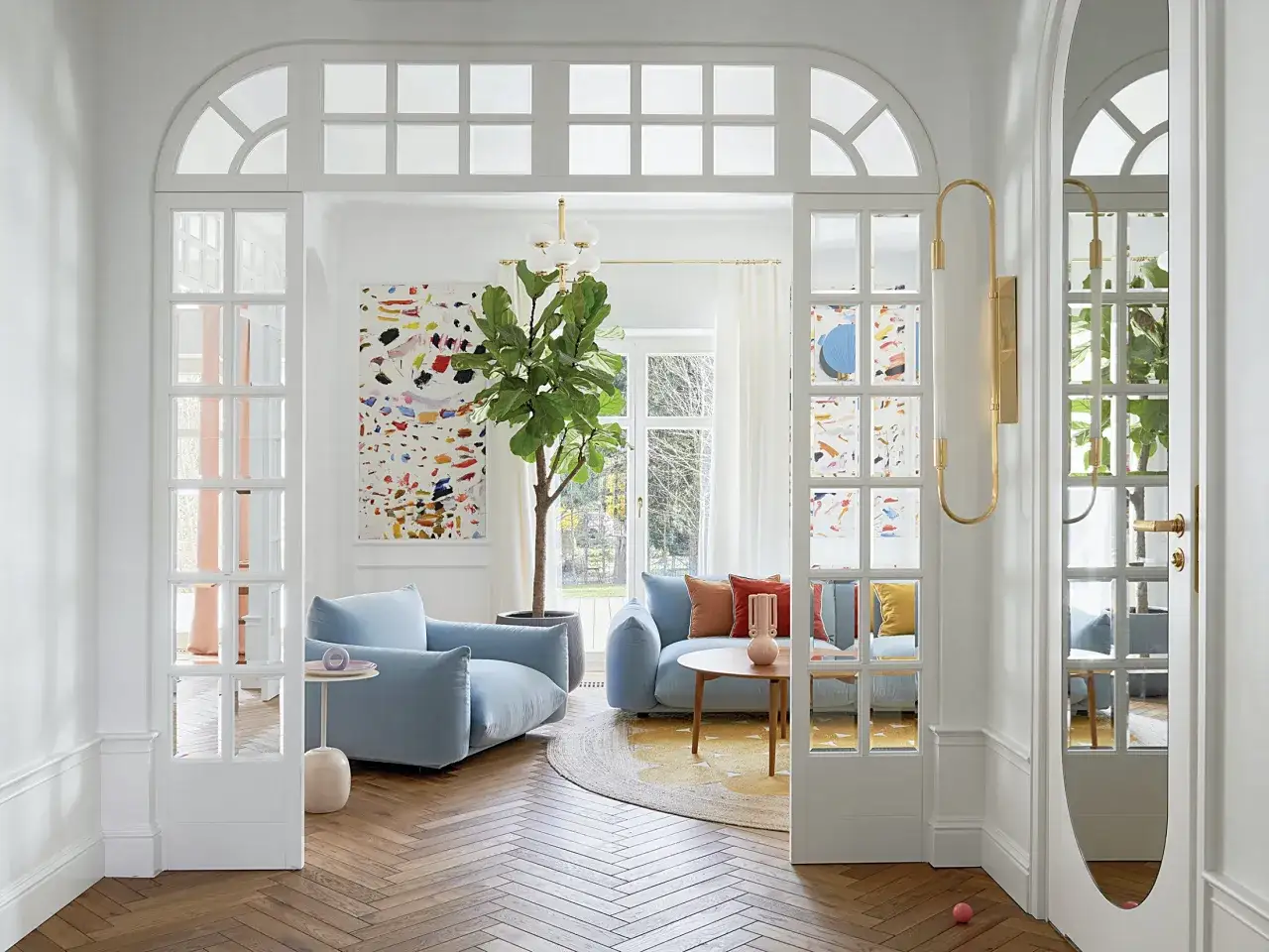 Jasny salon z błękitnymi sofami, kolorowym obrazem i dużą rośliną. Elegancki łuk w salonie inspiracje, dodaje lekkości.