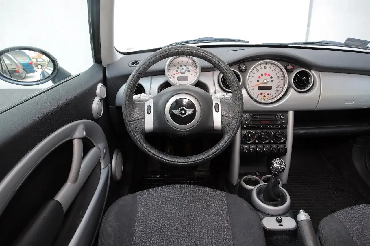 Wnętrze Mini Cooper R50: kierownica, deska rozdzielcza z okrągłymi zegarami, radio i dźwignia zmiany bieg&oacute;w.