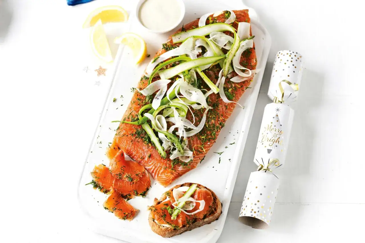 Saumon gravlax recette festive : un plat de saumon cru marin&eacute;, garni de l&eacute;gumes croquants, servi avec des toasts et des d&eacute;corations de No&euml;l.