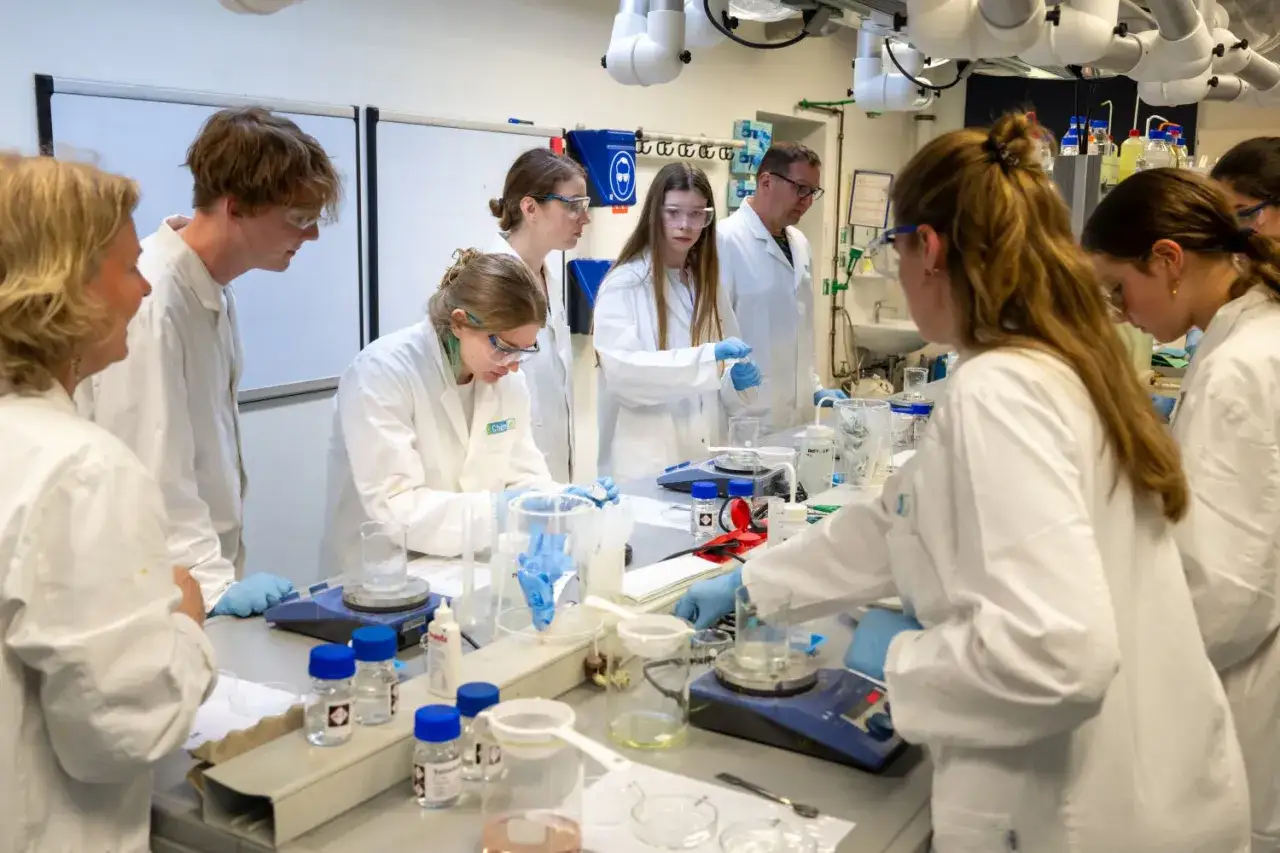Sch&uuml;ler experimentieren im Labor w&auml;hrend der Nacht der Wissenschaft Berlin. Sie tragen Laborkittel und Schutzbrillen und arbeiten mit verschiedenen Chemikalien und Ger&auml;ten.