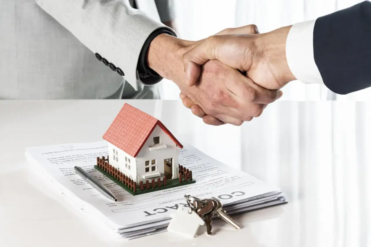 Accordo di permuta immobiliare con costruttore: stretta di mano, modello di casa, chiavi e contratto.