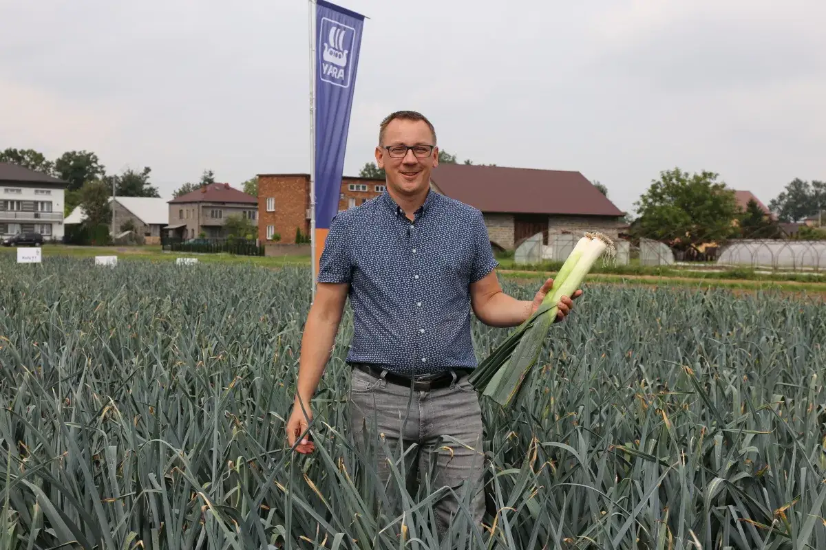 Rolnik z dumą prezentuje dorodne pory po obsypywaniu. W tle pola i budynki gospodarcze.