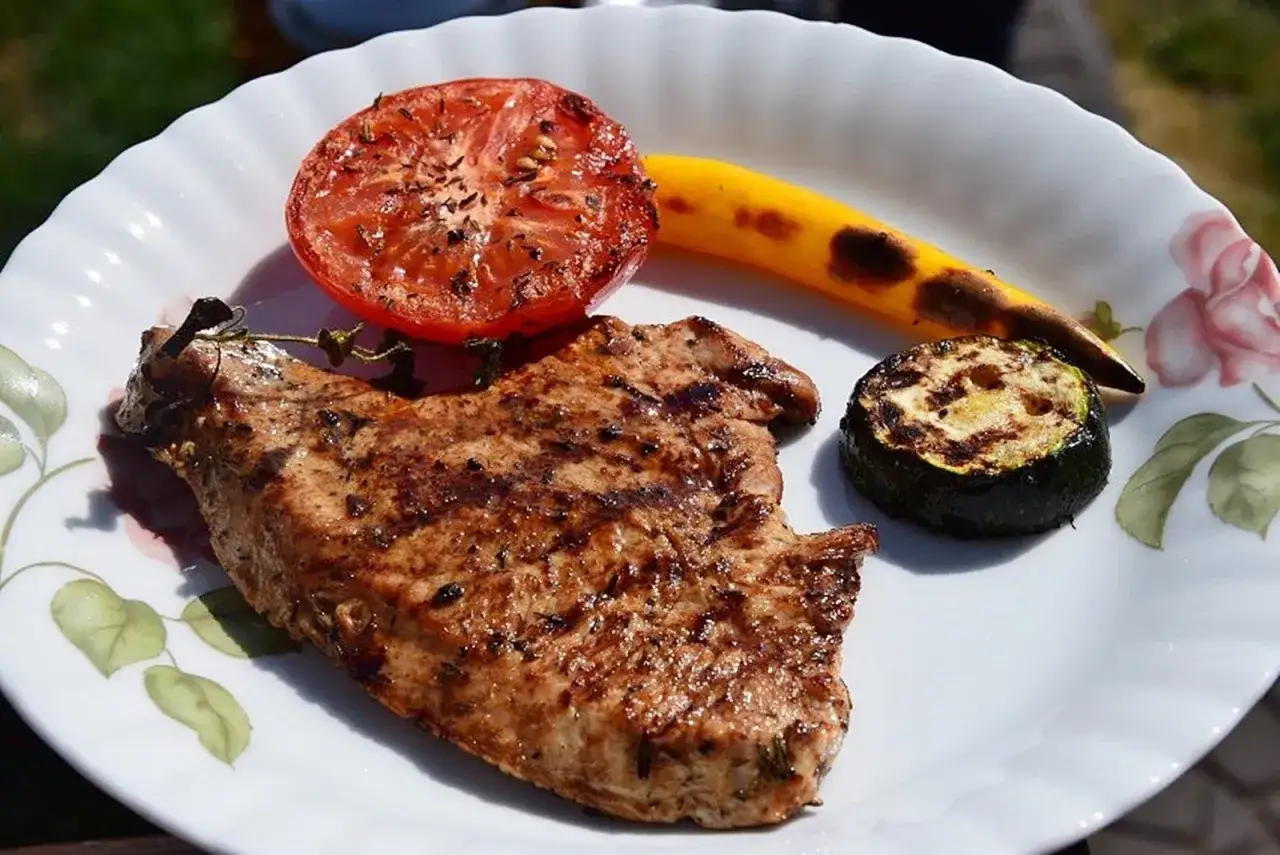 Grillowany kotlet z indyka, idealny po marynacie, z pomidorem, cukinią i papryką. Pyszny obiad na talerzu.