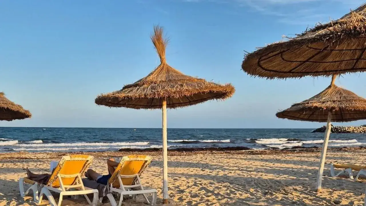 Słońce nad plażą w Tunezji, idealne miejsce na relaks jak u Marco Polo. Dwa leżaki pod słomianymi parasolami, morze i błękitne niebo.