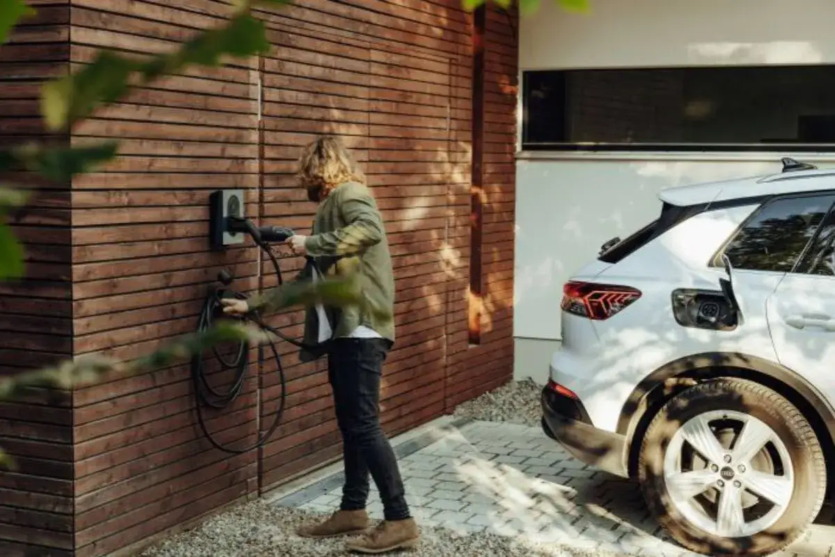 Mężczyzna podłącza biały samochód elektryczny do ładowarki. Zastanawiasz się, jaki prąd do ładowania samochodu elektrycznego będzie najlepszy?