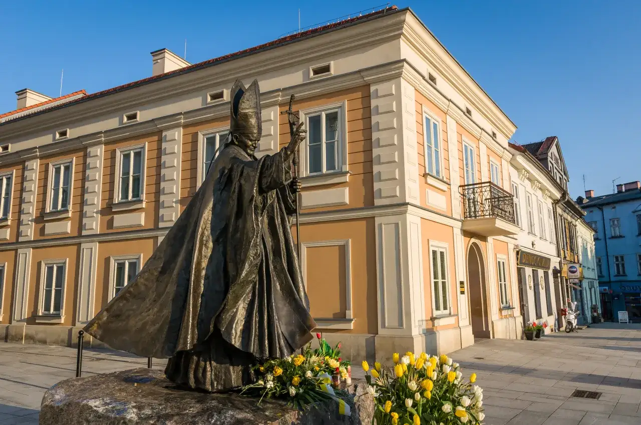 Pomnik Jana Pawła II na rynku w Wadowicach, idealne miejsce do zwiedzania. W tle kamienice i błękitne niebo.