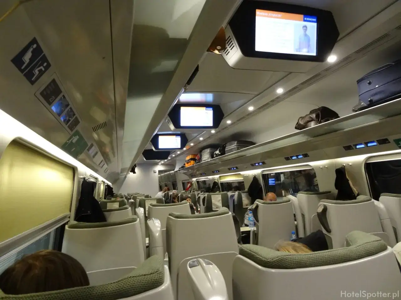 Wnętrze Pendolino z wygodnymi fotelami, ekranami informacyjnymi i bagażami na półkach.