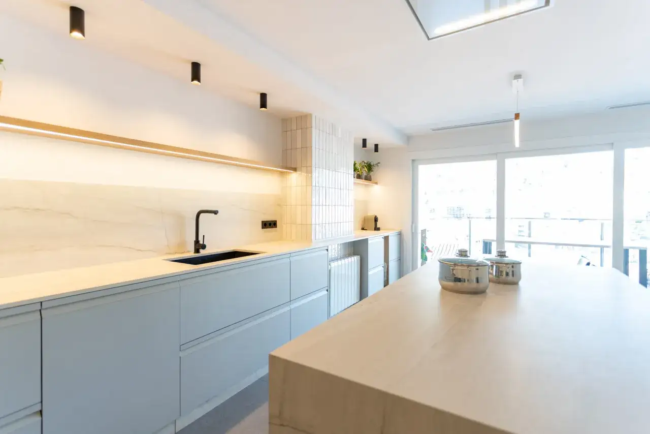 Moderna cocina con isla central, gabinetes grises, encimeras de m&aacute;rmol y grandes ventanales.