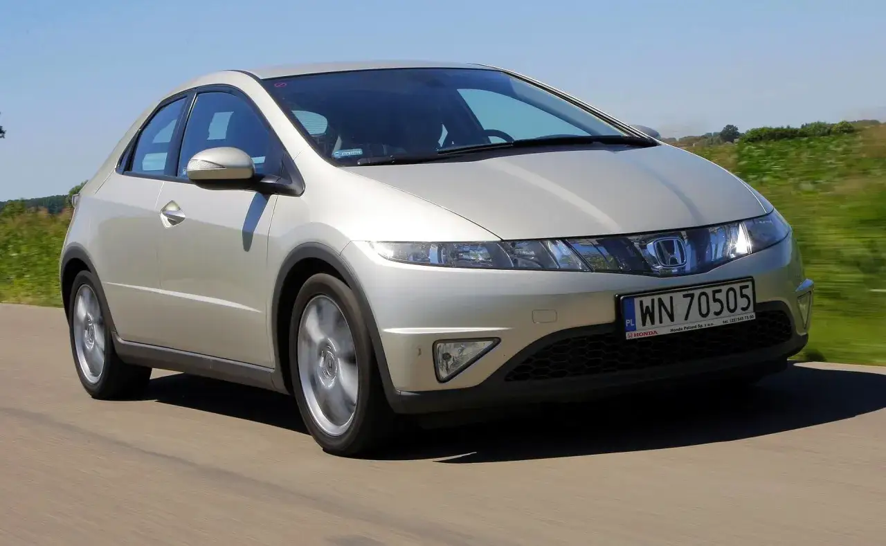 Srebrny Honda Civic, wyglądający jak UFO, pędzi po drodze wśród zielonych pól.