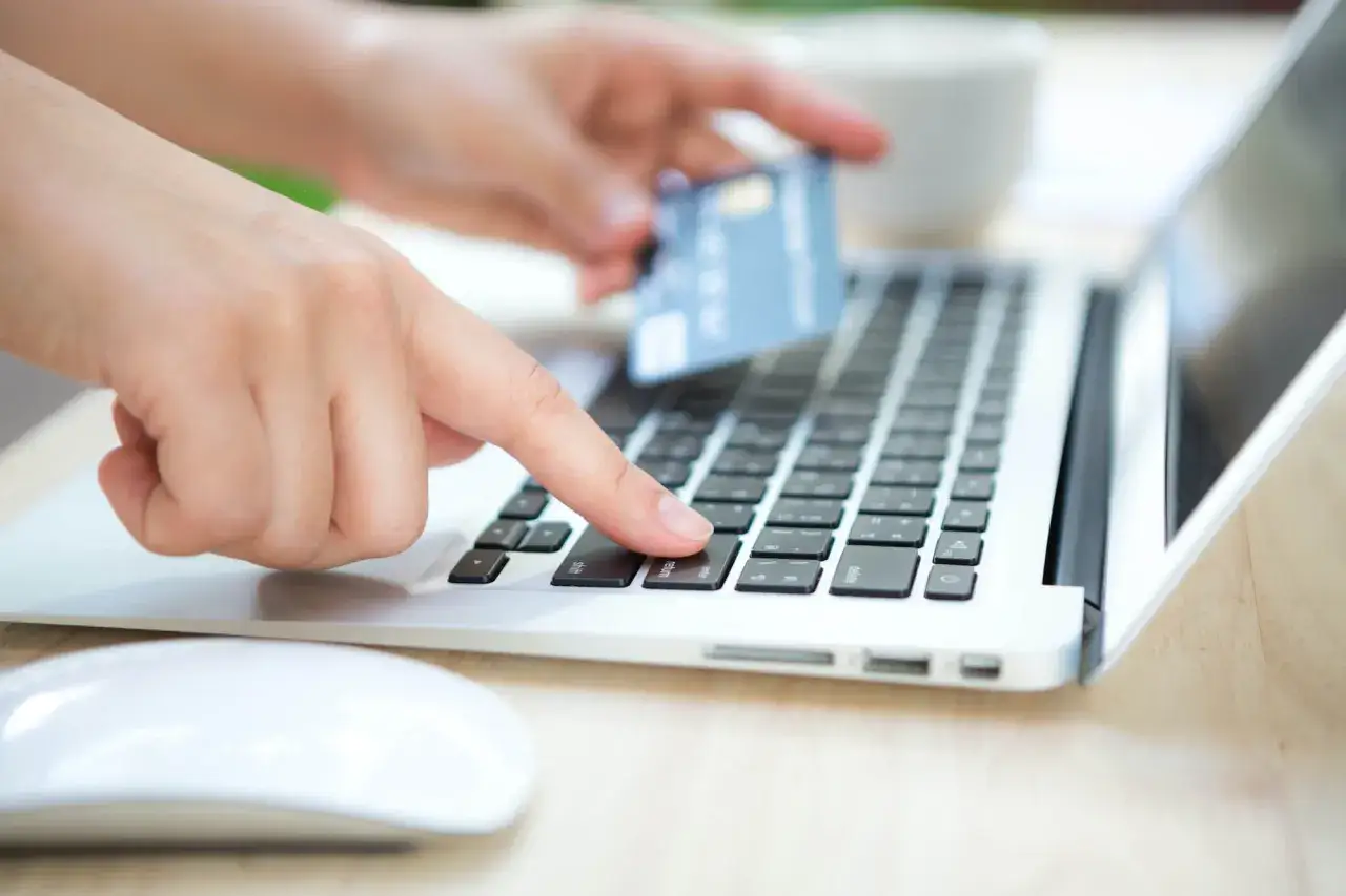 Dłoń z kartą zbliża się do klawiatury laptopa. Czy Skrill jest bezpieczny? Pytanie o bezpieczeństwo płatności online.