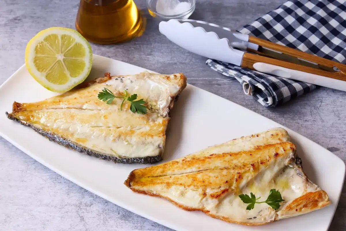 Dos filetes de dorada a la plancha, jugosos y dorados, servidos con perejil fresco y una rodaja de lim&oacute;n.