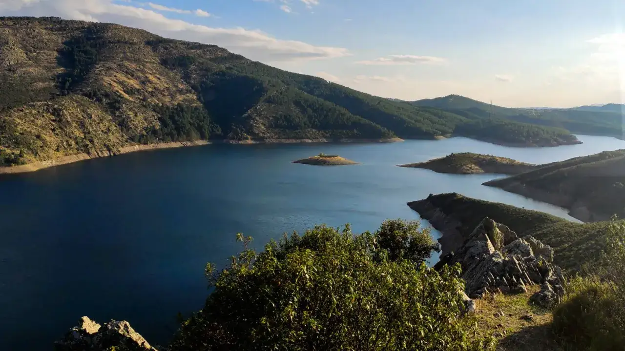 La senda del Genaro serpentea entre montañas y un lago azul profundo, con una pequeña isla en el centro.