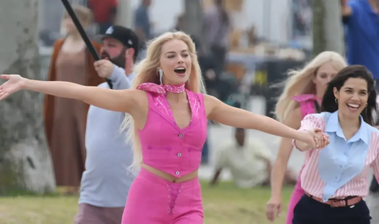 Margot Robbie jako Barbie w różowym stroju, z radością biegnie z innymi kobietami.