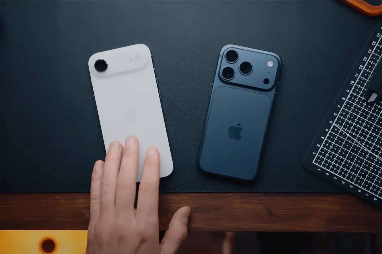 Deux iPhones, un blanc et un bleu nuit, pos&eacute;s sur un bureau. Une main effleure le mod&egrave;le blanc, pr&ecirc;t &agrave; d&eacute;couvrir la nouveaut&eacute; iPhone.