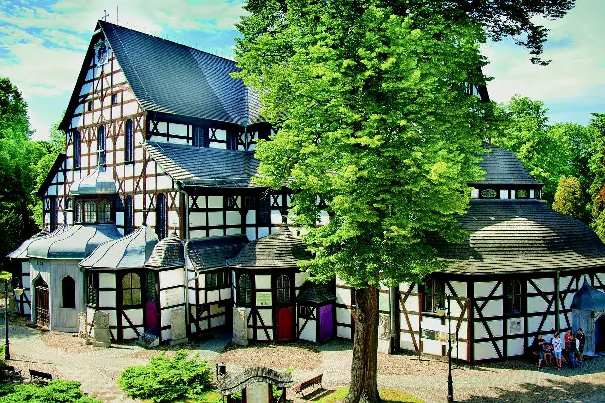 Drewniany kościół w stylu szachulcowym, jeden z wielu ciekawostek o Polsce. Otoczony zielenią, z charakterystyczną architekturą.
