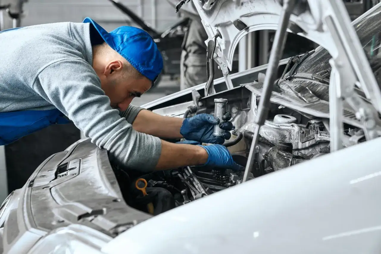 Mecánico con guantes azules realiza mantenimiento de motores, concentrado en el interior del vehículo.