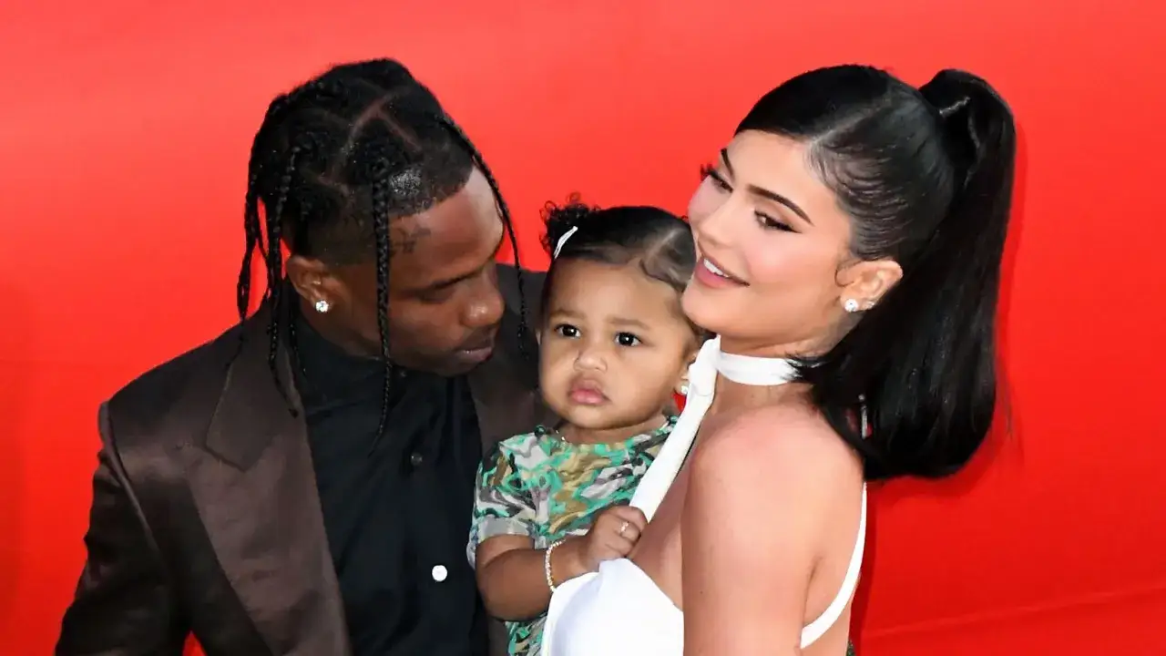 Travis Scott i Kylie Jenner z córką Stormi Webster na czerwonym tle.