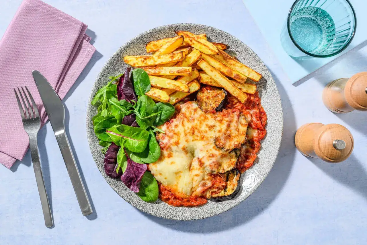 En tallrik med aubergineparmigiana, en fräsch sallad och gyllene pommes frites. Perfekt för en mysig middag.