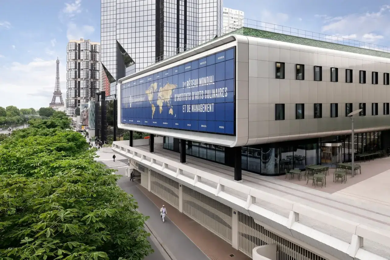 Le Cordon Bleu Paris, un réseau mondial d'instituts culinaires, s'affiche fièrement sur un bâtiment moderne, avec la Tour Eiffel en arrière-plan.